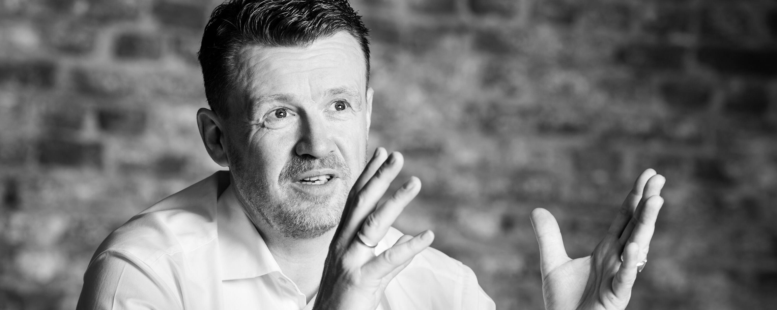 Zwart-witfoto van Raymond Löhr in gesprek, die met beide handen een punt uitlegt